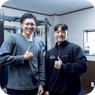 トレーナーと利用者がジム内で並んでポーズを取っている様子